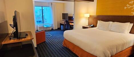 A hotel room with a bed, desk, chair, and a view of the outside.