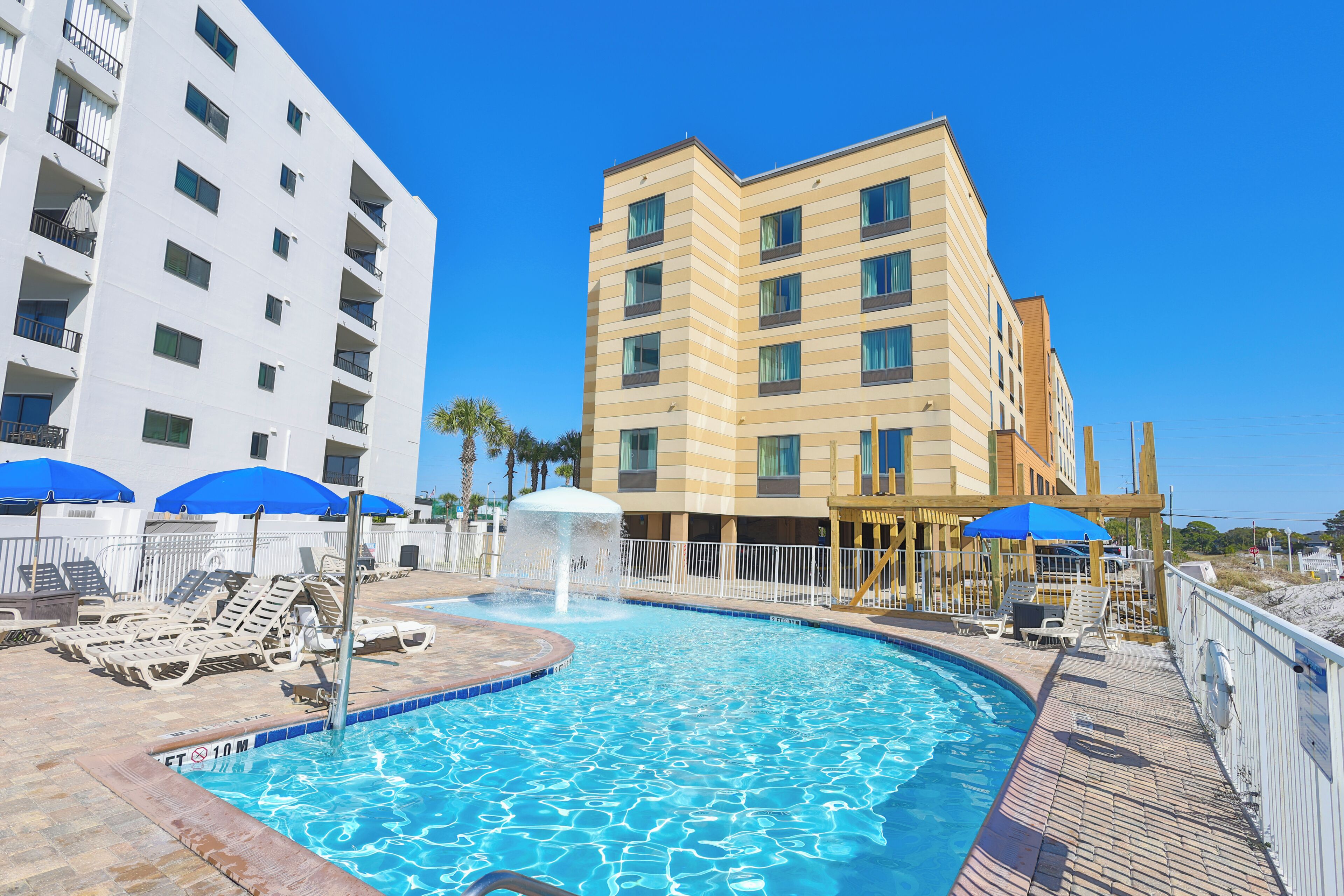 A swimming pool with lounge chairs and umbrellas, surrounded by multi-story buildings.