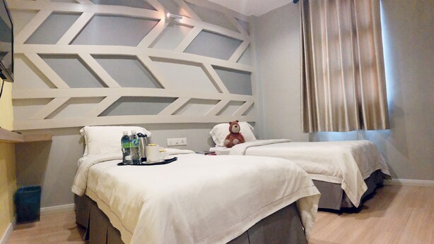 Une chambre d’hôtel avec deux lits, un plafond décoratif, une fenêtre avec des rideaux et une petite poubelle.