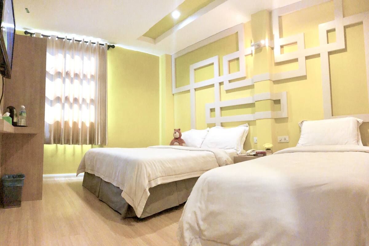 A hotel room with two beds, a wooden cabinet, a trash bin, and a curtain.