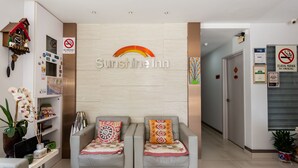 Un espace d’accueil avec deux canapés gris, une enseigne fixée au mur indiquant « Sunshine Inn », et un panneau « Interdiction de fumer ».