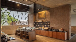 A modern breakfast bar with a brick wall backdrop, a large window with a view of palm trees, and a variety of breakfast items displayed.
