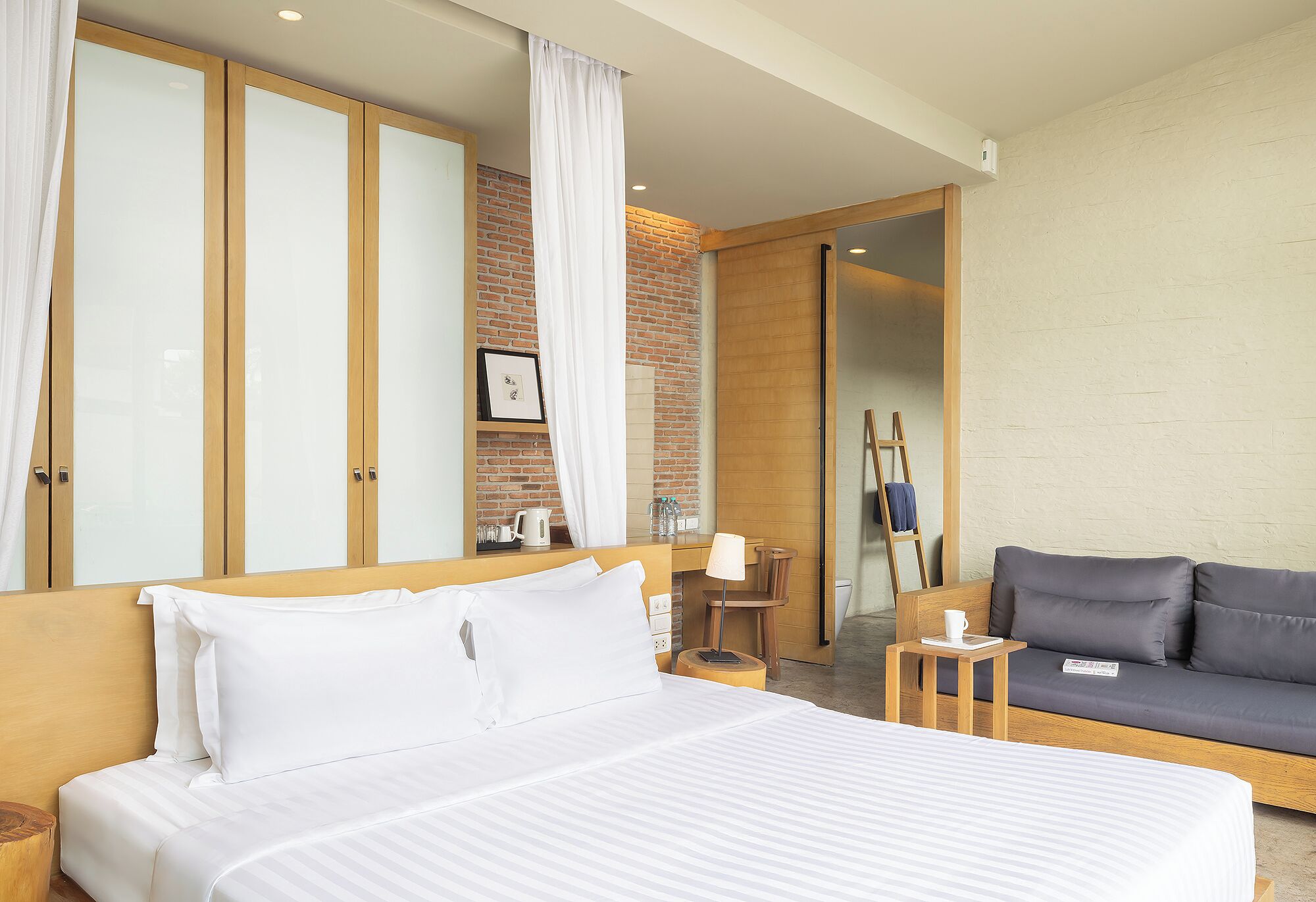 A hotel room with a bed, a sofa, a desk, and a mirror.