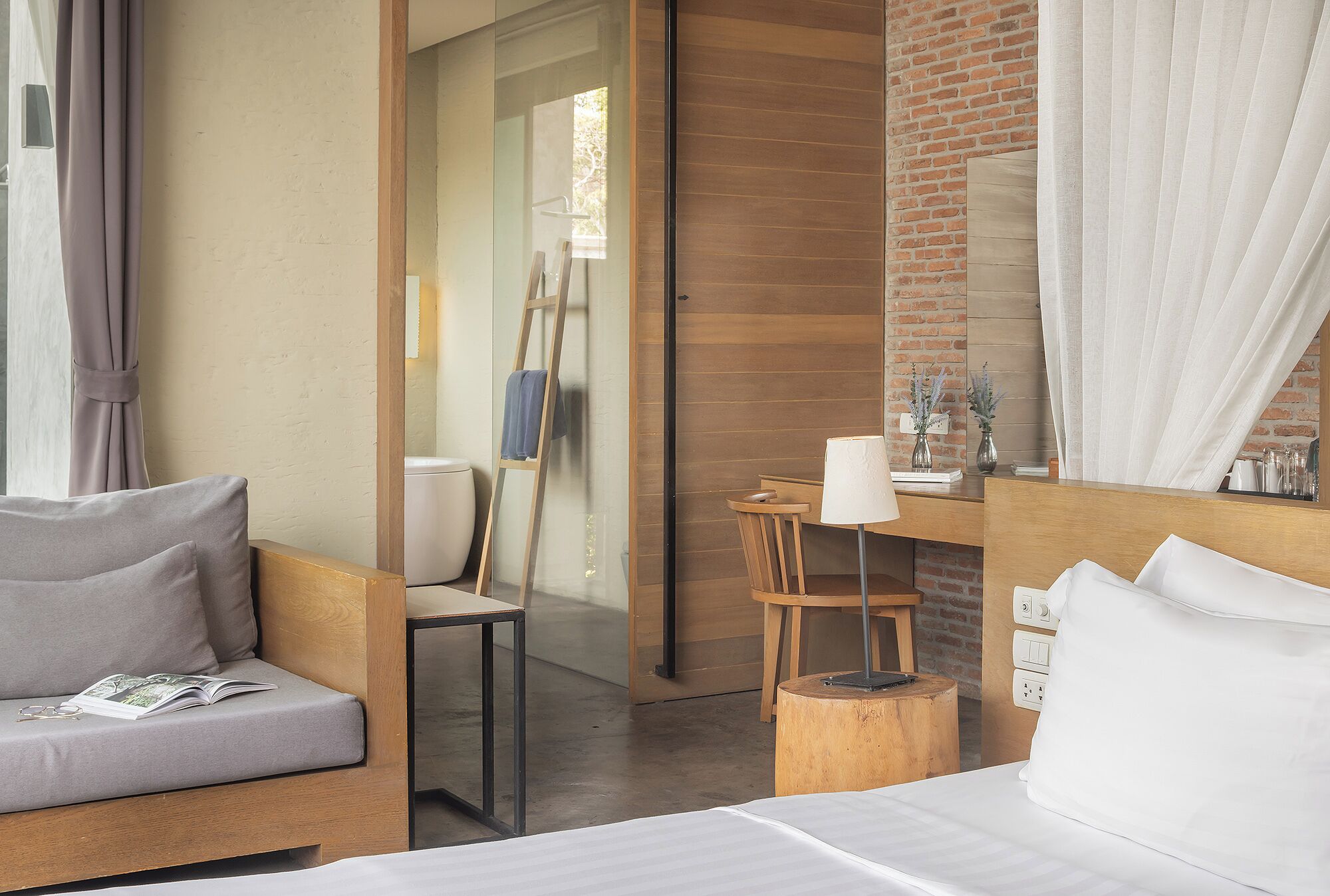 A modern hotel room with a wooden bed, a sofa, a desk with a lamp, and a chair.