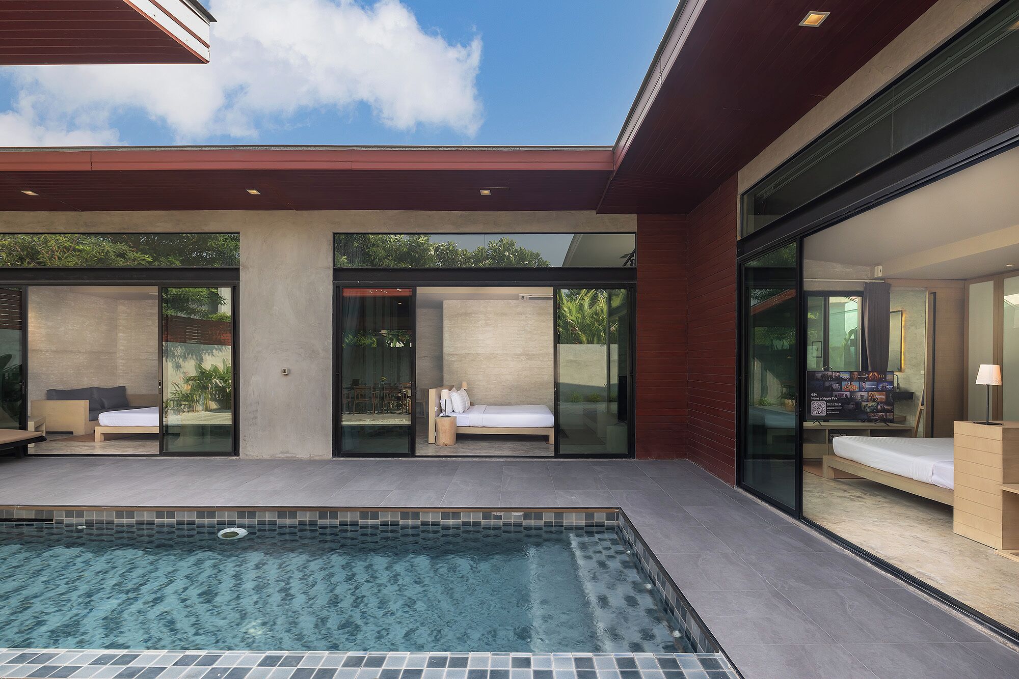 A modern outdoor pool area with glass walls, a lounge chair, and a small seating area.