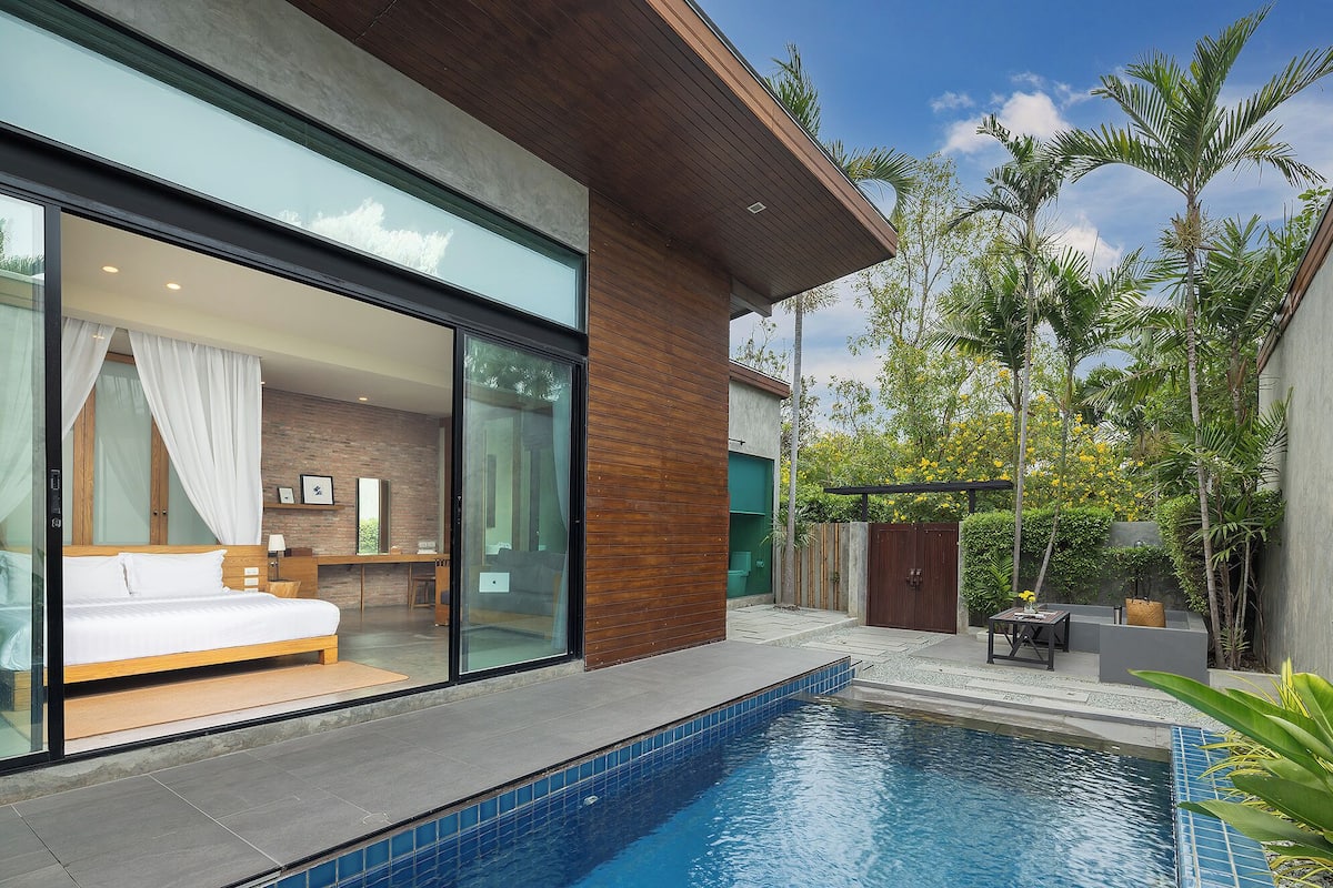 Une chambre d’hôtel moderne dotée d’une grande fenêtre en verre, d’un lit et offrant une vue sur l’espace piscine.