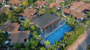 An aerial view of a resort with multiple bungalow-style buildings, a central swimming pool, and lush greenery.