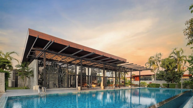 A modern pool area with a covered seating area, clear blue pool, and surrounding greenery.