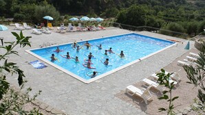Una piscina rodeada de sillas de descanso y sombrillas, con montañas al fondo.