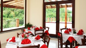 Comedor con mesas dispuestas para cuatro, ventanas amplias con vistas a zonas verdes y una estructura de pérgola de madera.