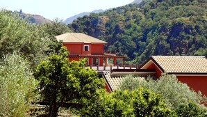 Una villa roja con techo de tejas, rodeada de abundante vegetación y colinas al fondo.