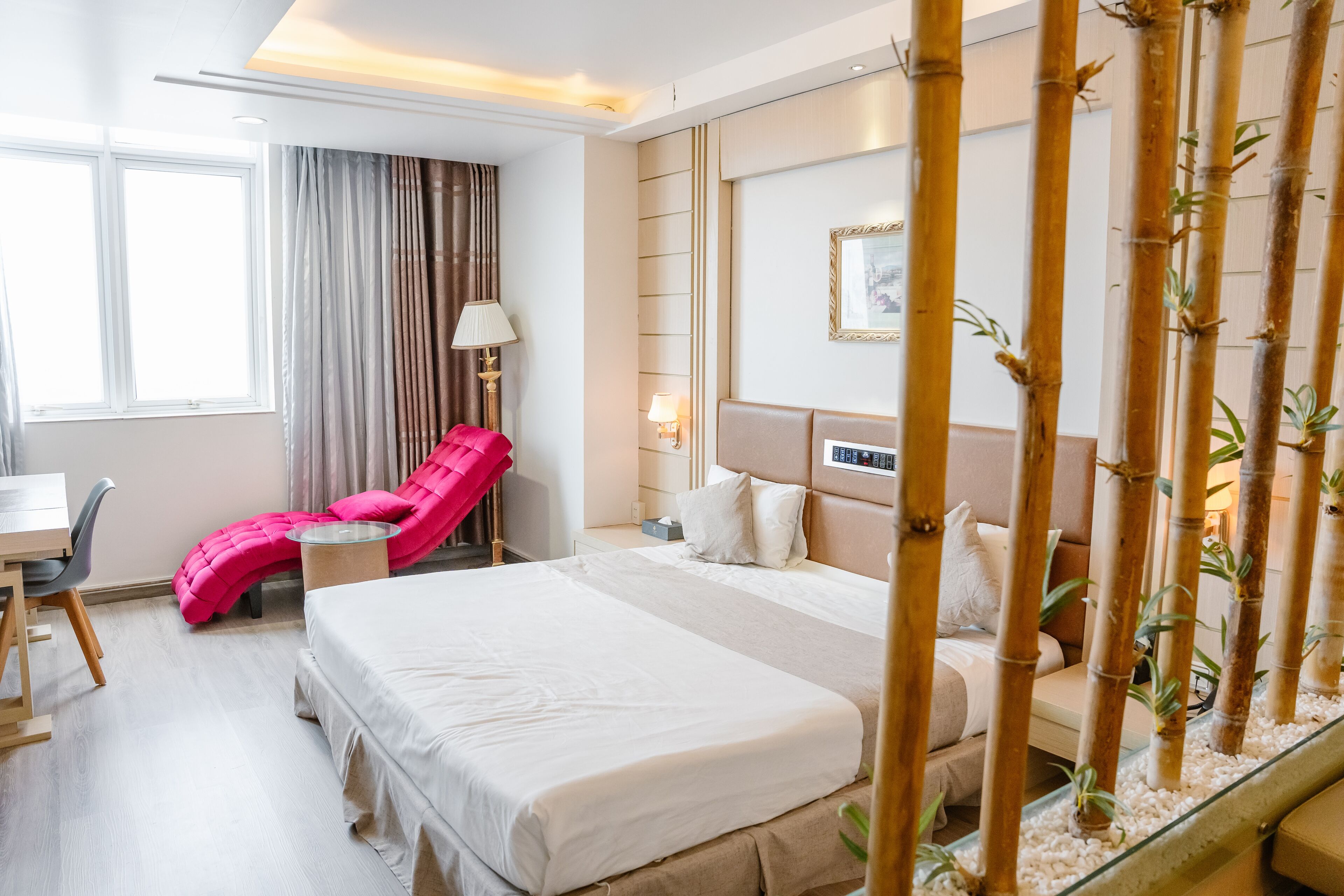 A hotel room with a bed, a desk, a chair, a massage chair, and a bamboo plant.