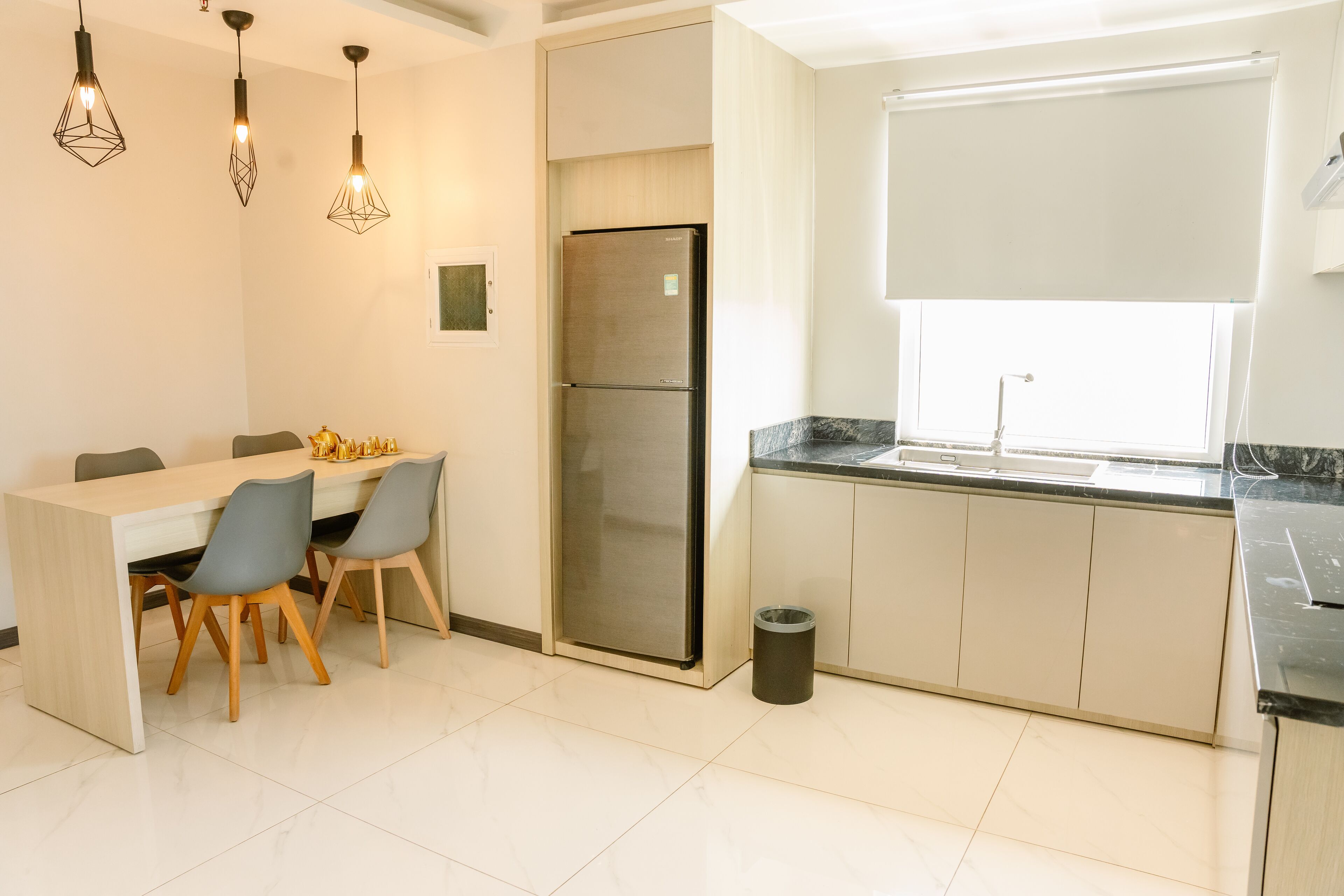 A modern kitchen with a dining area, stainless steel refrigerator, and pendant lighting.