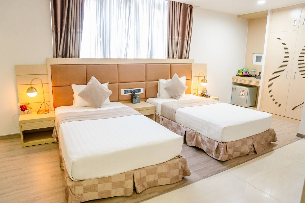 Une chambre d’hôtel avec deux lits, une petite kitchenette et une vue sur la ville grâce à de grandes fenêtres.