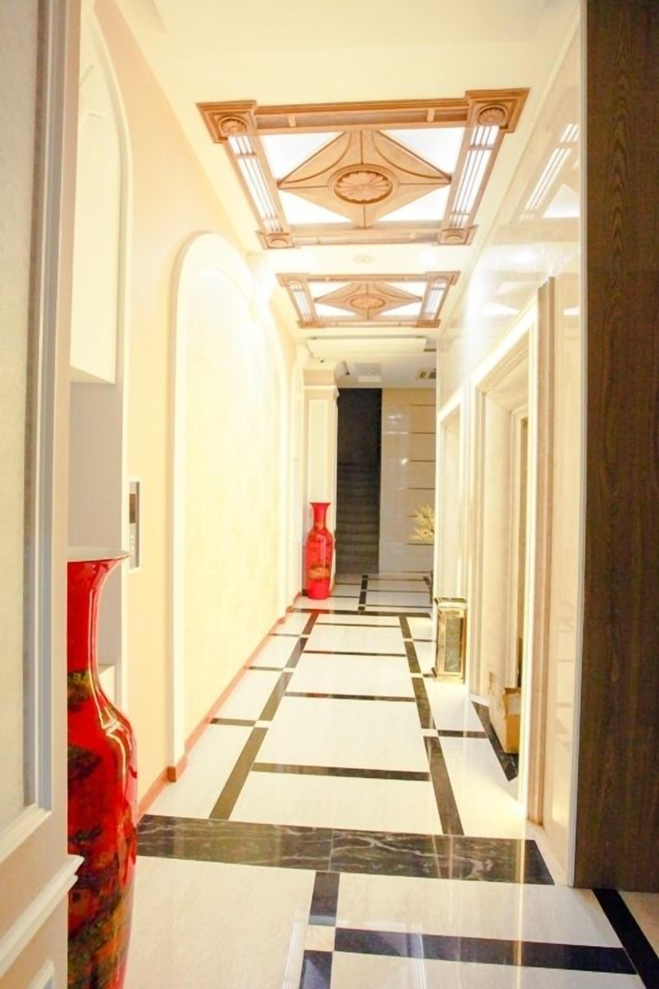 A hallway with a checkered floor, a red vase, and a ceiling with a geometric design.