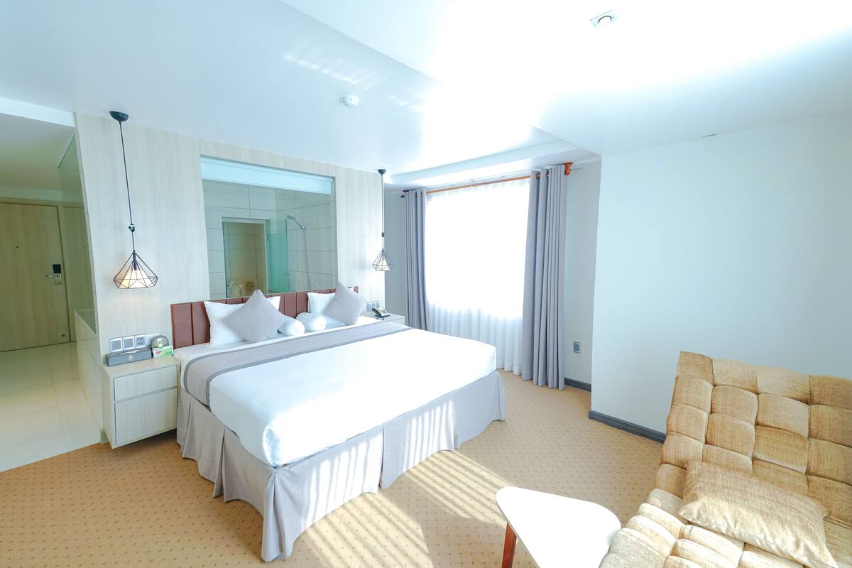Une chambre d’hôtel moderne avec un grand lit, un coin salon, un miroir et une fenêtre avec des rideaux.