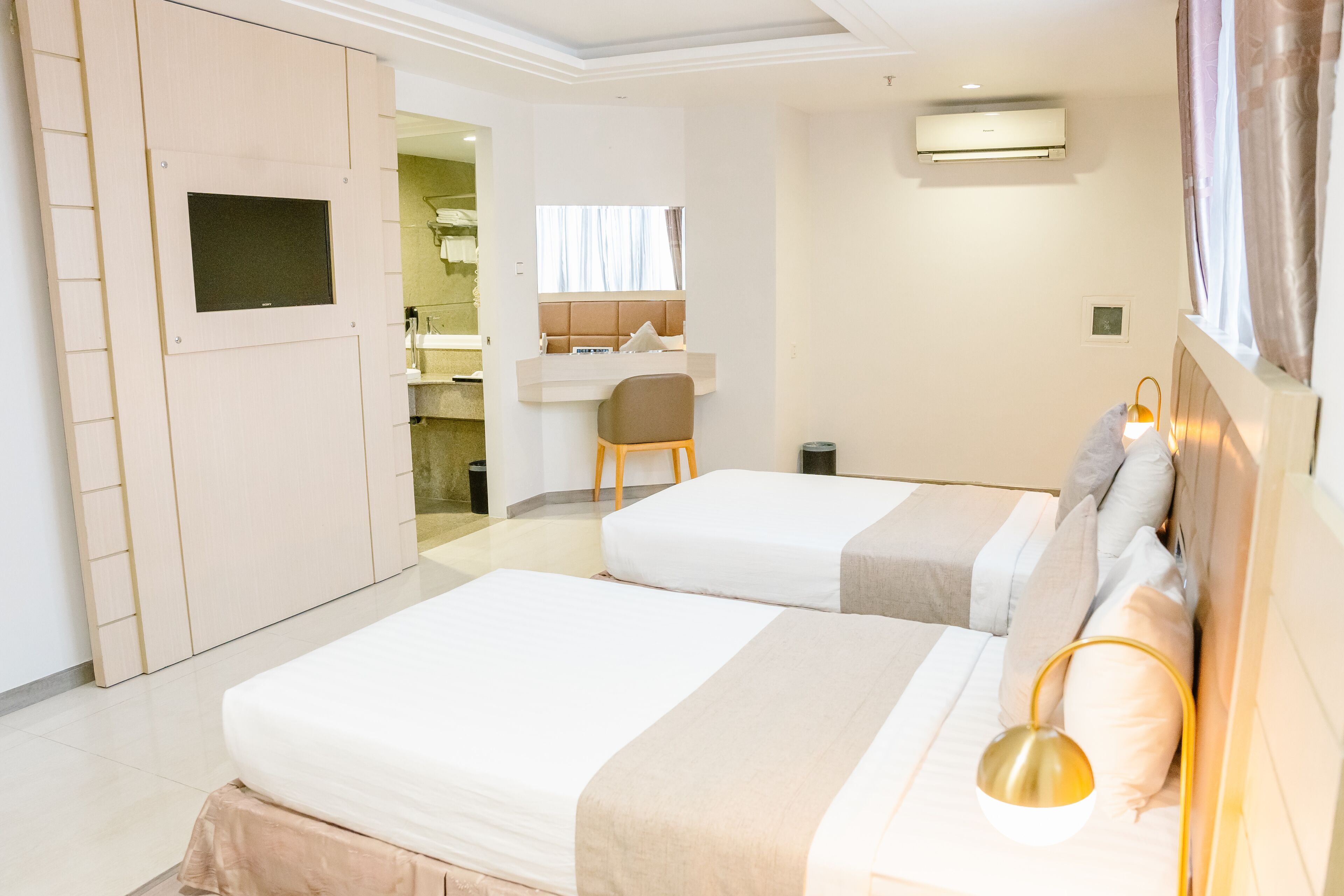 Une chambre d’hôtel avec deux lits, un bureau, une chaise, une armoire et un appareil de climatisation.