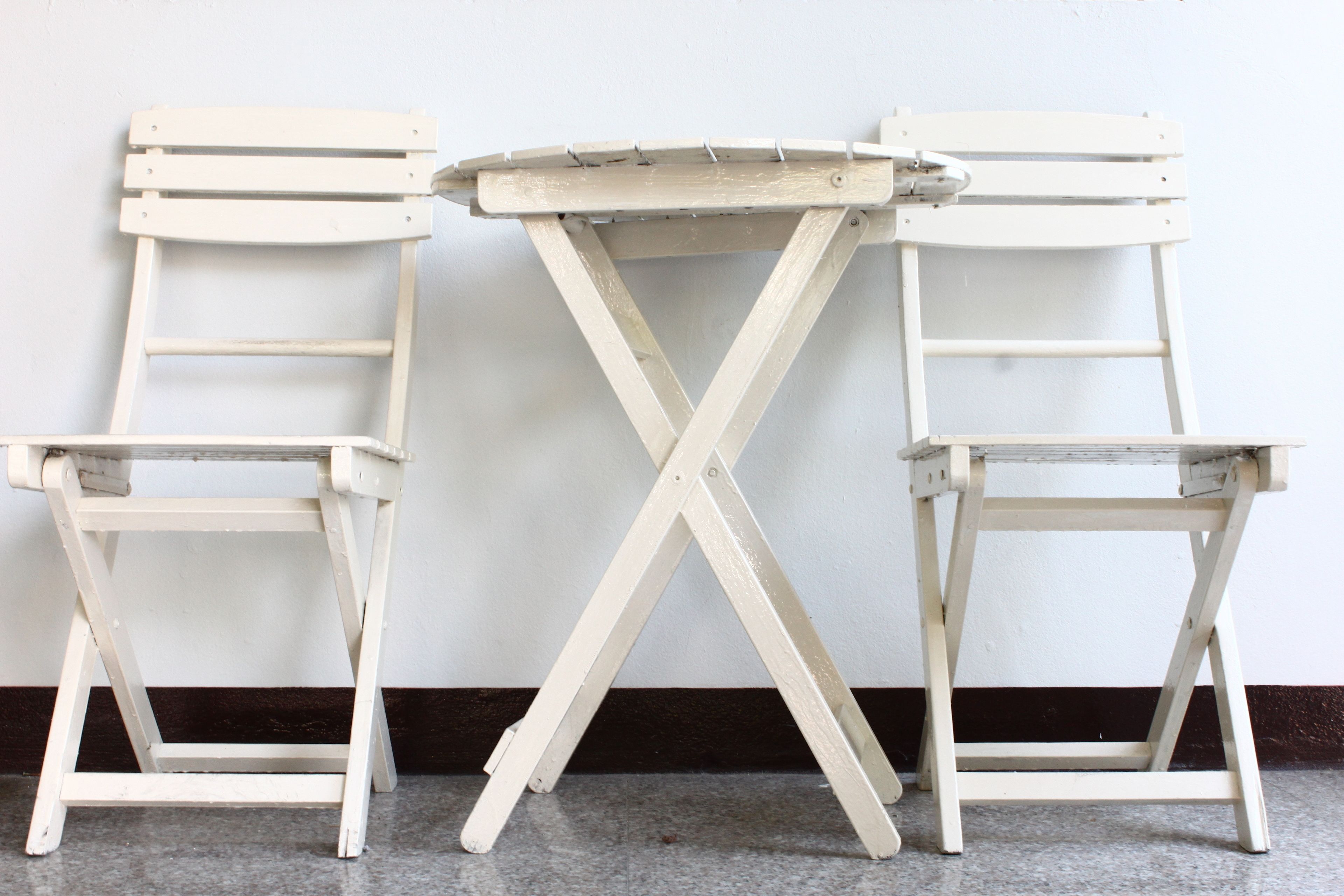 Une table pliante blanche, accompagnée de deux chaises, est placée contre un mur uni.