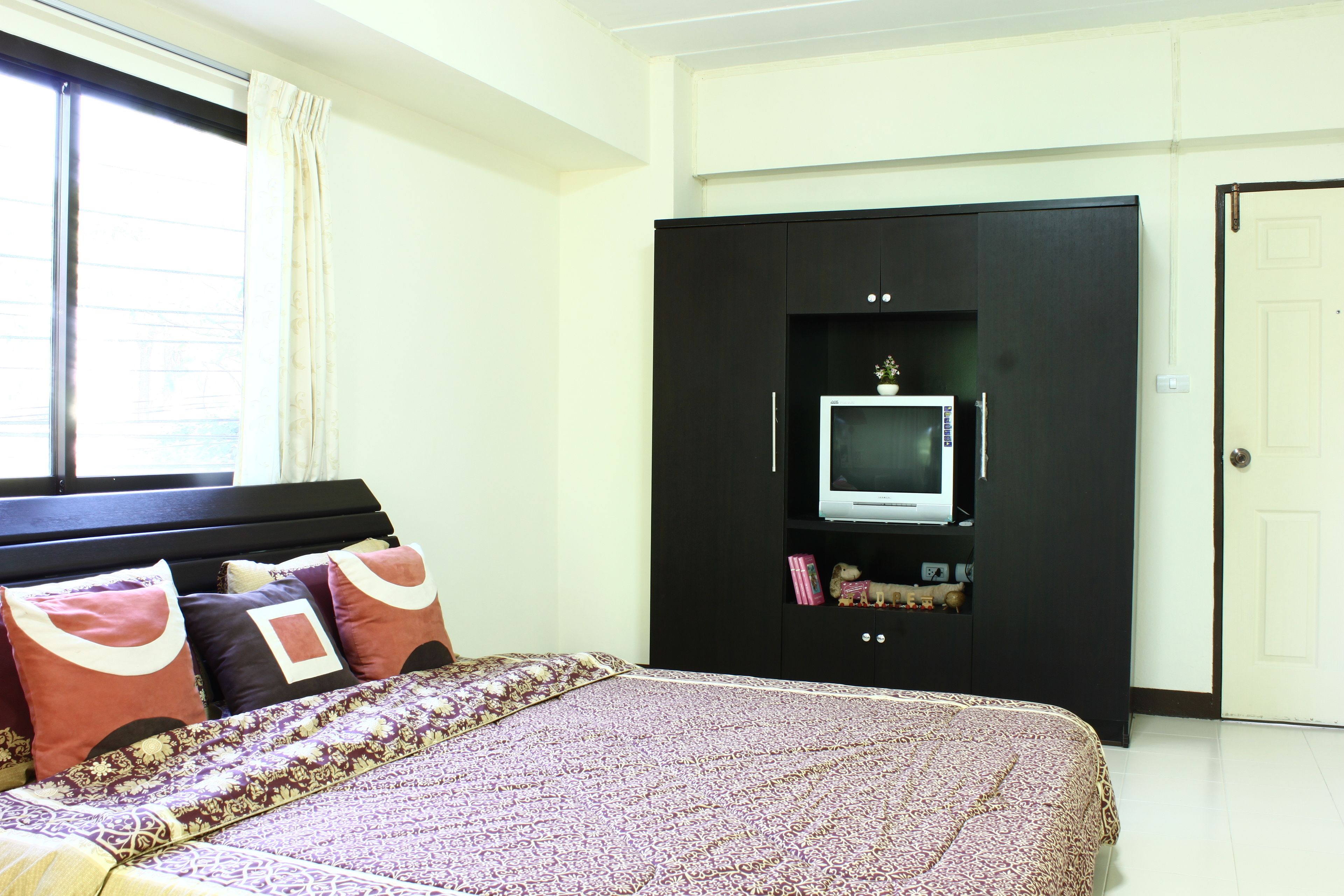 A bedroom with a bed, a wardrobe, a television, and a window with curtains.