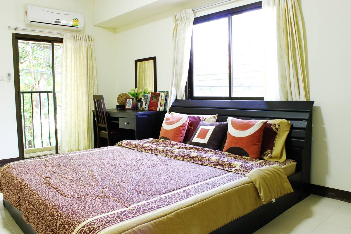 A bedroom with a bed, a desk, and a window with curtains.