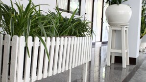 A white picket fence planter with green plants, a white pedestal pot, and a polished floor. - The European Place (Bangkok)
