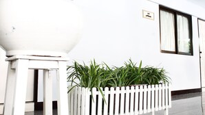 A white building with a white picket fence, a potted plant, and a door with a window. - The European Place (Bangkok)