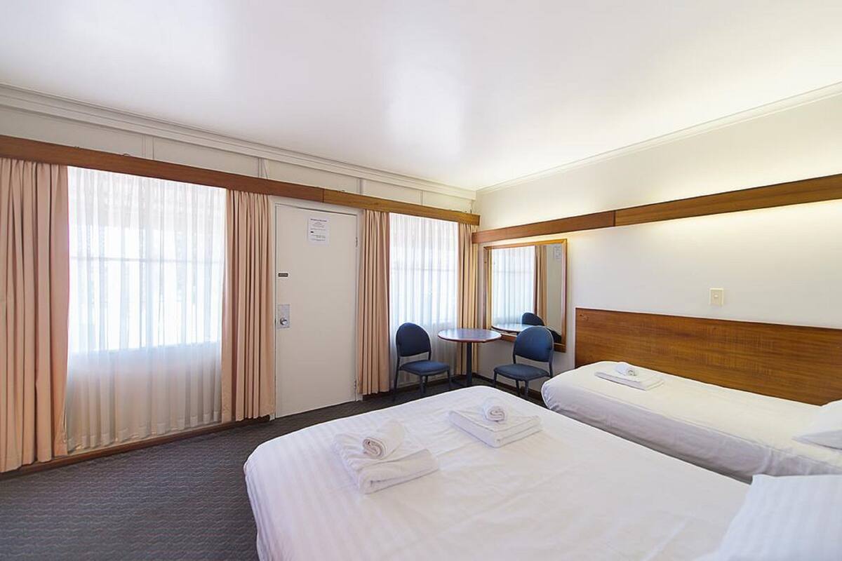 A hotel room with two beds, a small table, two chairs, and a window with curtains.
