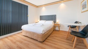 A modern hotel room with a bed, bedside table, chair, and a small table with a lamp. - Blue Hills Motel (Battery Point)