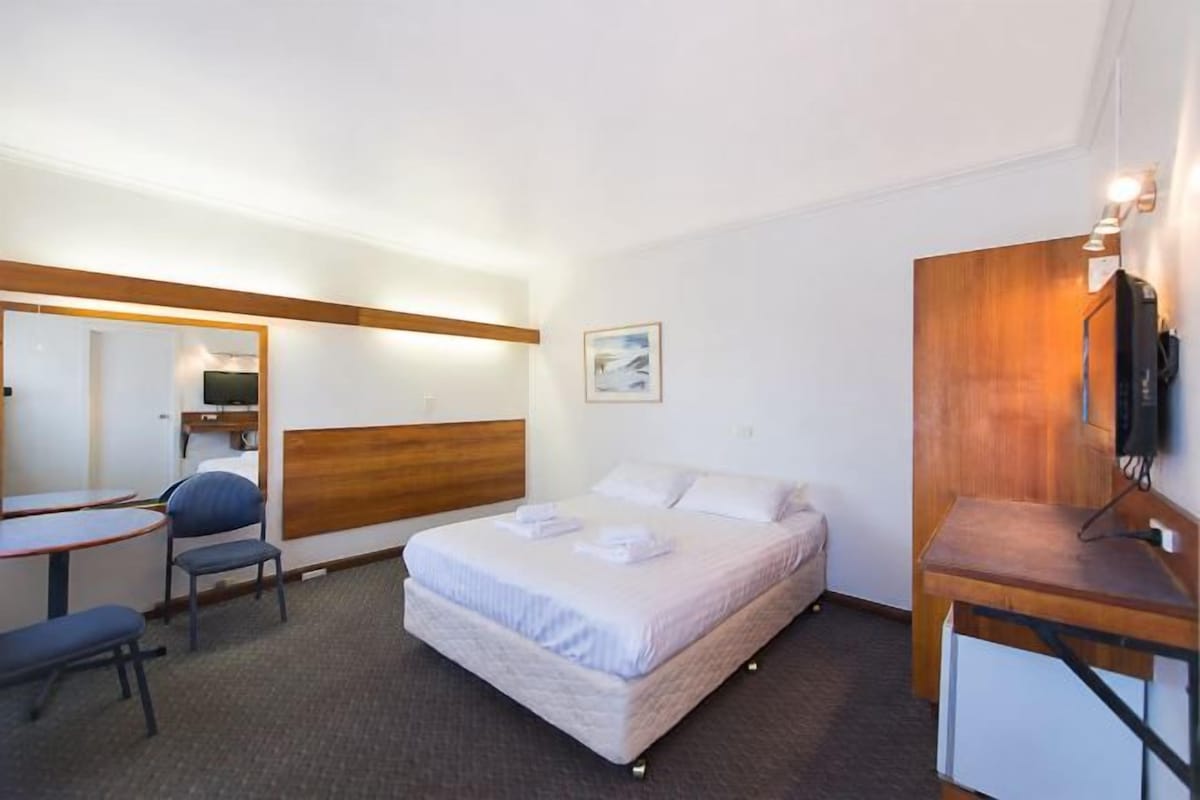 A hotel room with a bed, a desk, a chair, a television, and a mirror.