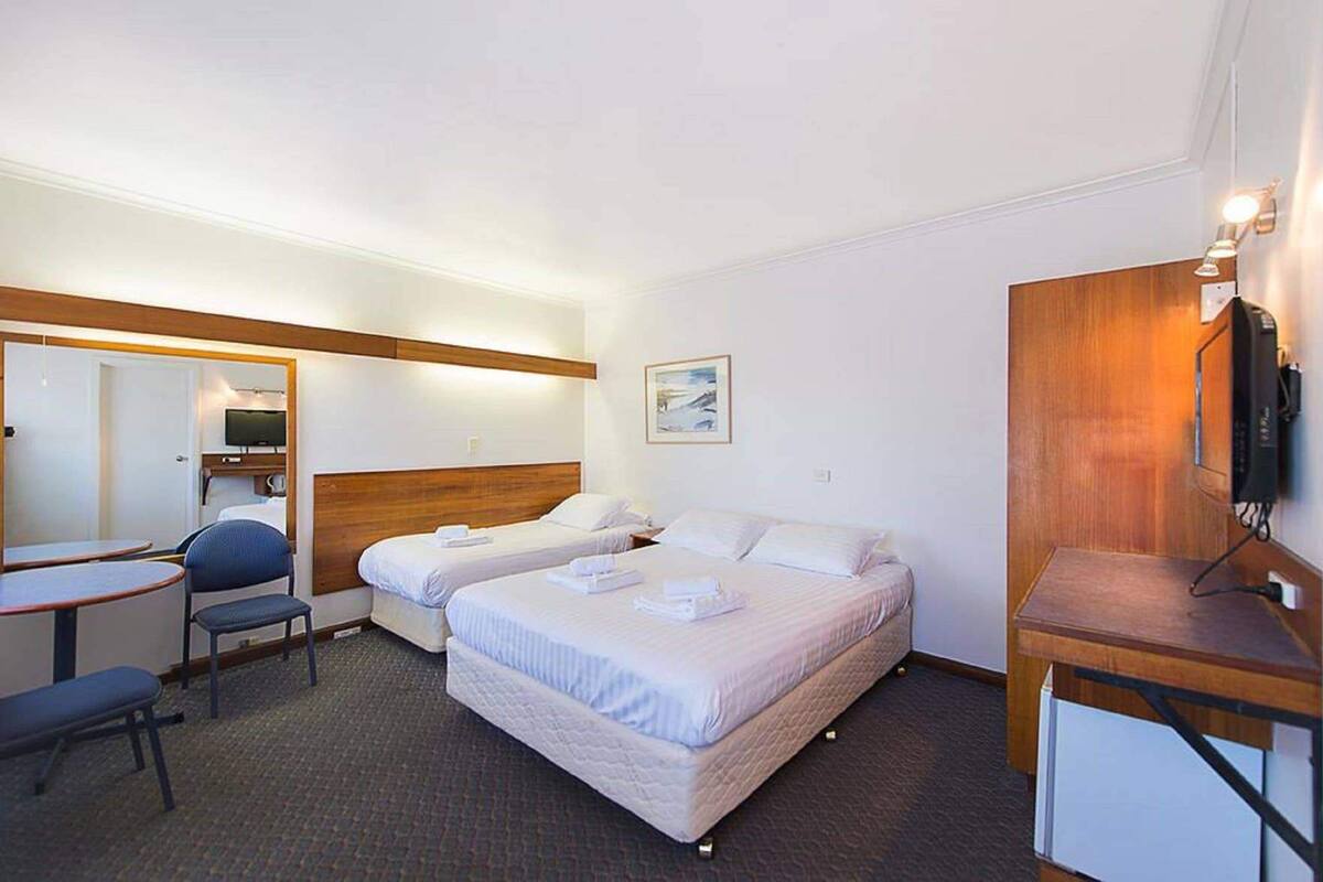 A hotel room with two beds, a desk, a chair, a television, and a wooden panel on the wall.