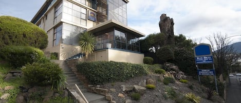 Um edifício moderno de dois andares com fachada de vidro, escadaria de pedra e um jardim bem cuidado.