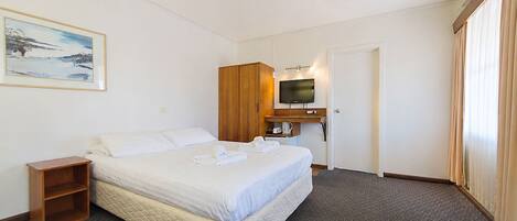 A hotel room with a bed, a television, a wooden wardrobe, a small table, and a painting on the wall.
