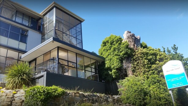 A modern building with large glass windows, a balcony, and a sign for Blue Hills Motel. - Blue Hills Motel (Battery Point)