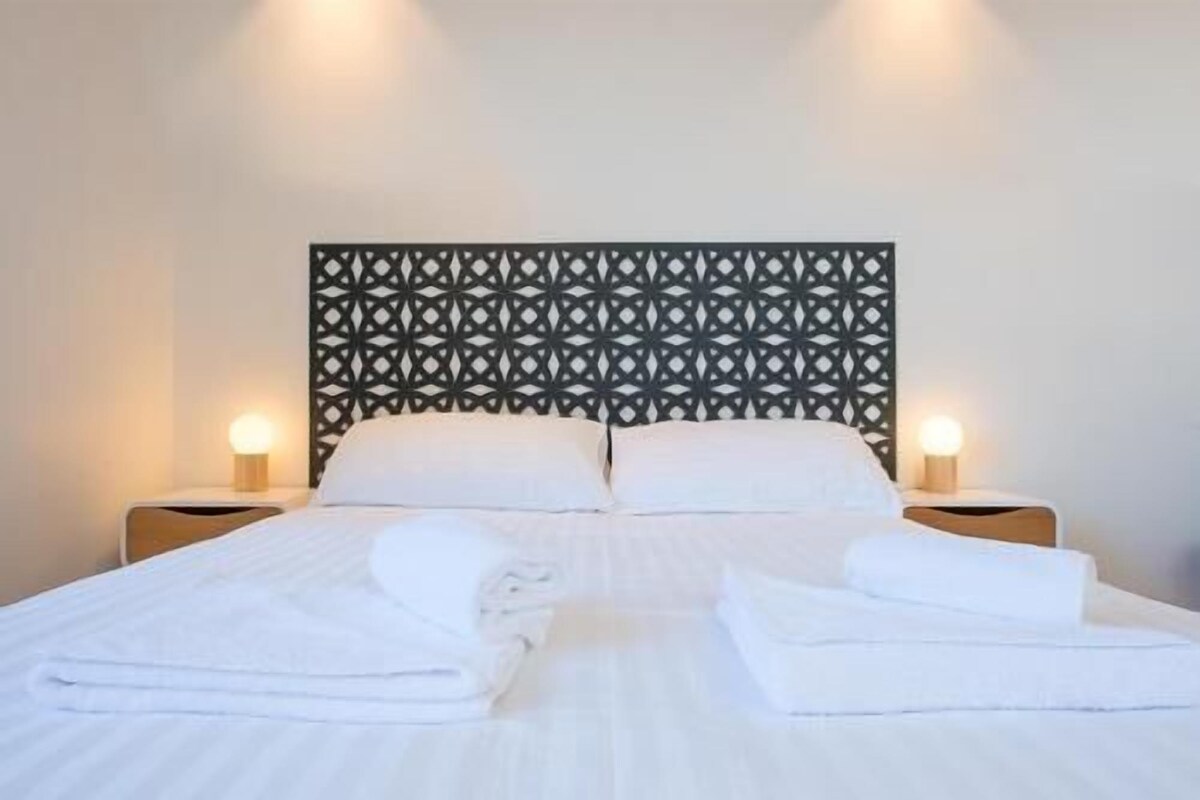 A neatly made bed with white linens, two bedside tables with lamps, and a decorative headboard.