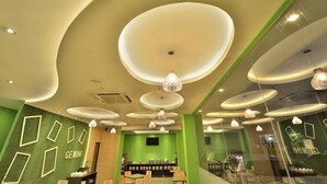 A modern interior with a green wall, multiple seating areas, and a central counter. - Zodiak MT Haryono by KAGUM Hotels (Jakarta)