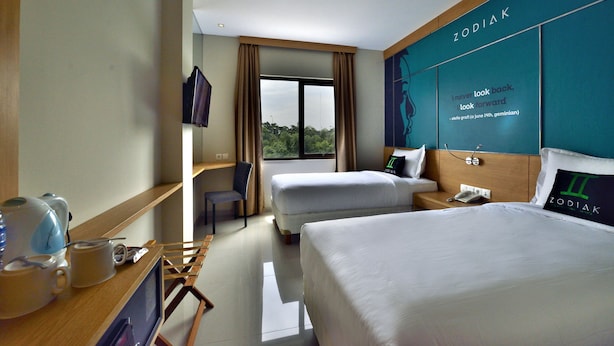 A hotel room with two beds, a desk with a chair, a TV, and a window with curtains. - Zodiak MT Haryono by KAGUM Hotels (Jakarta)