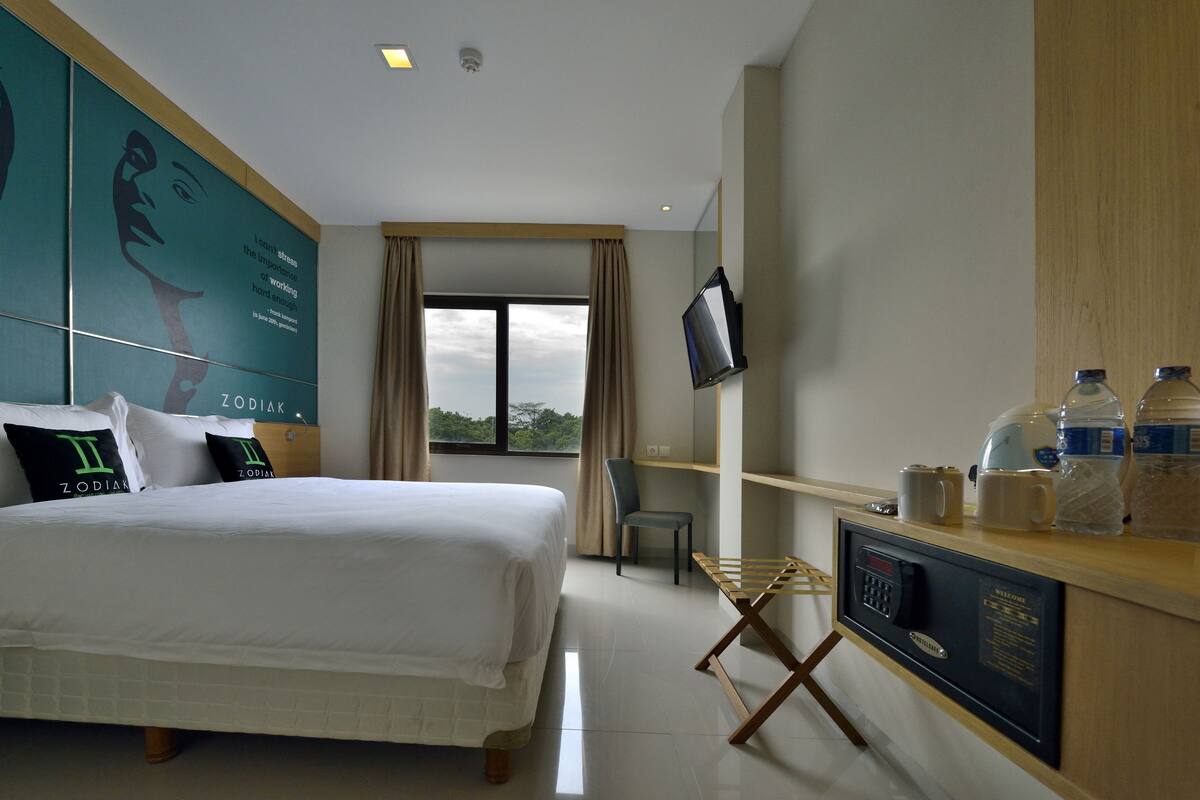 A hotel room with a bed, a desk with a computer, a chair, and a TV.