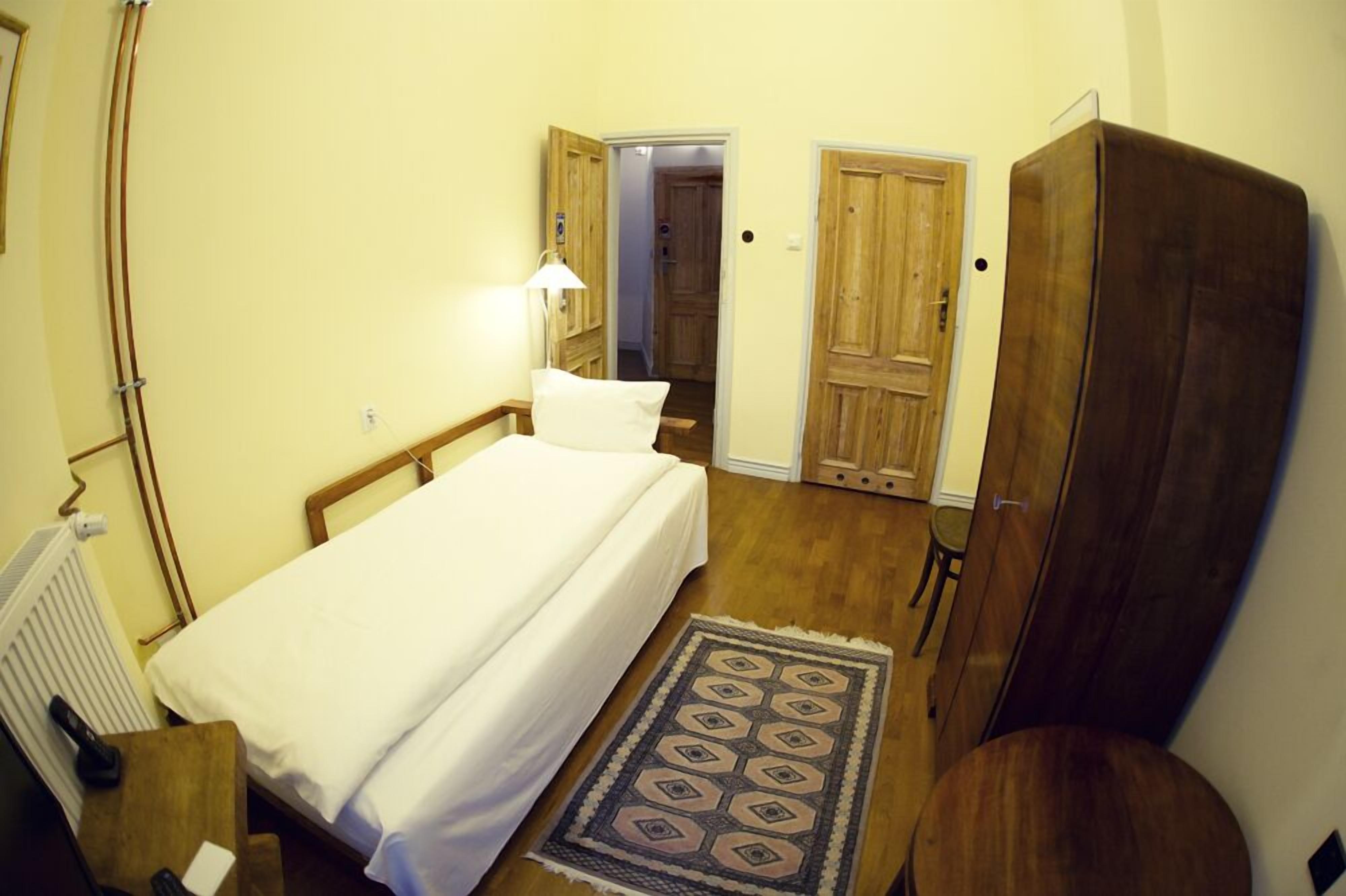 Un dormitorio pequeño y acogedor con una cama individual, un armario de madera, una mesita y una lámpara.