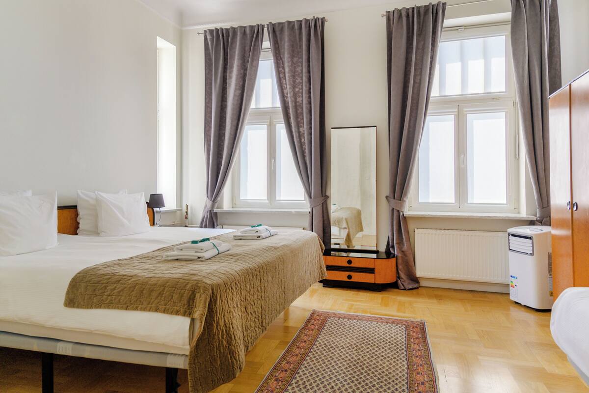 A hotel room with a bed, a dresser, a mirror, a heater, and a window with curtains.