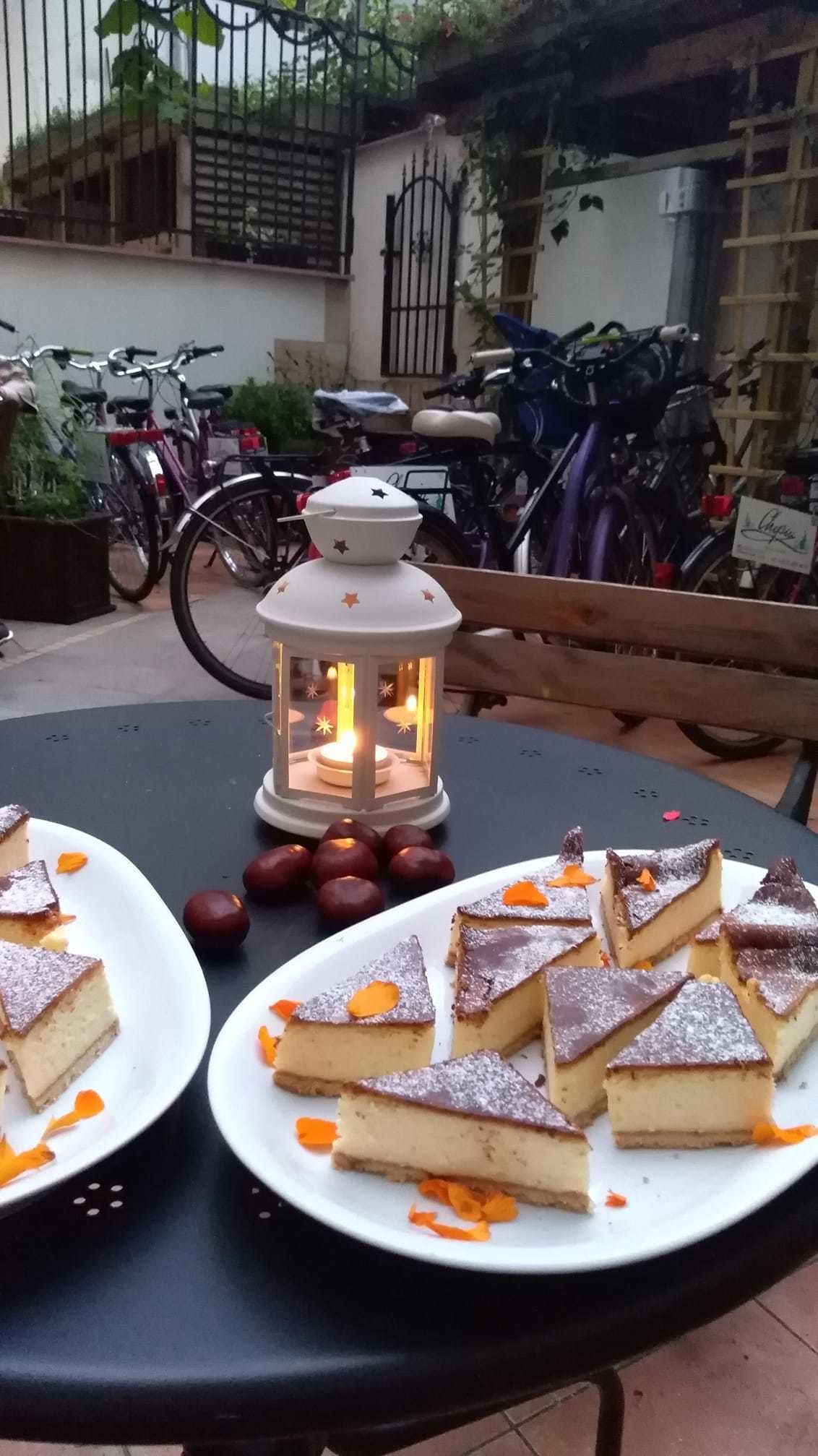 A table with plates of dessert, a lantern, and parked bicycles in the background.