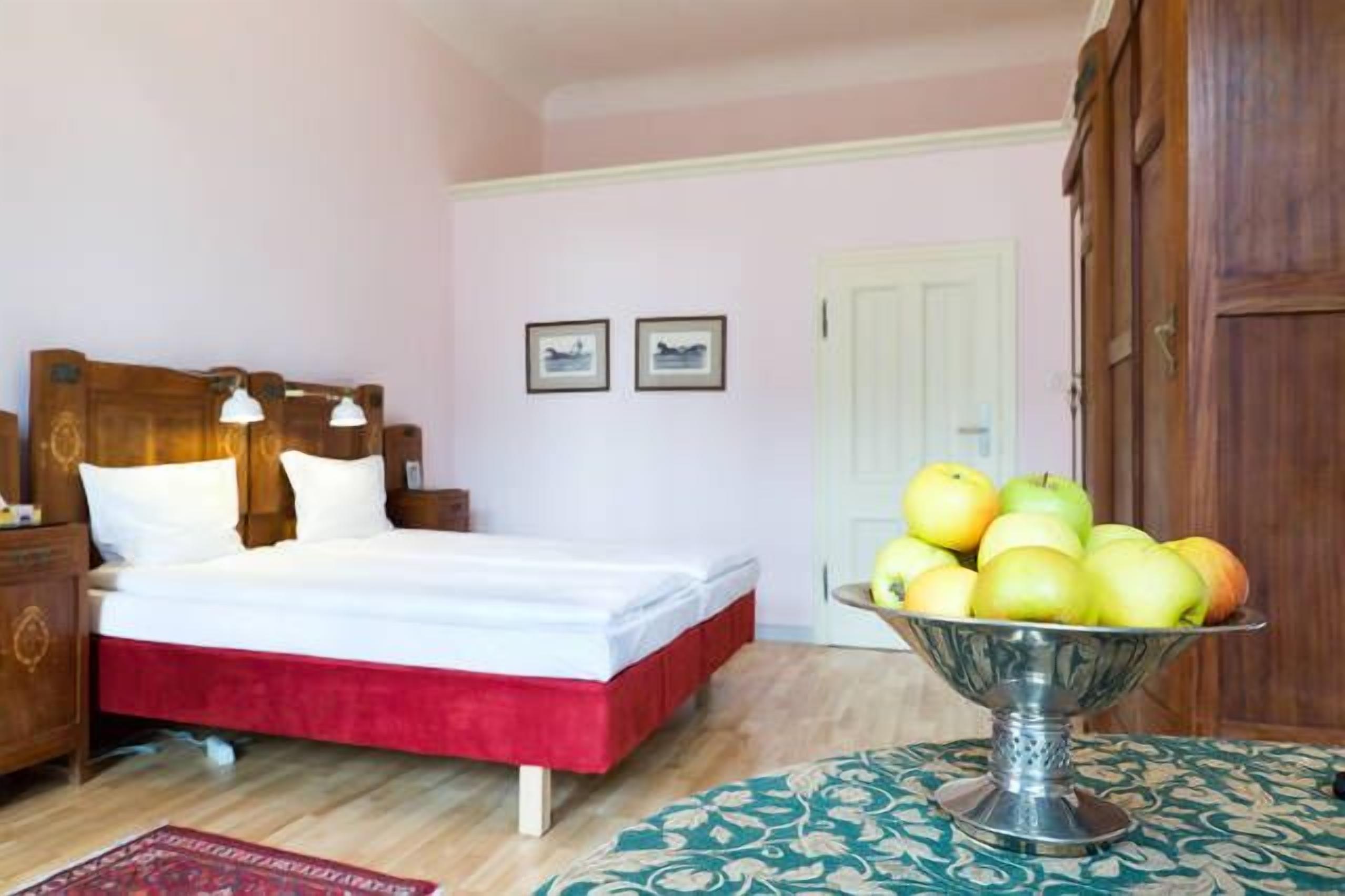 A bedroom with a bed, bedside table, lamp, and a fruit bowl on a table.