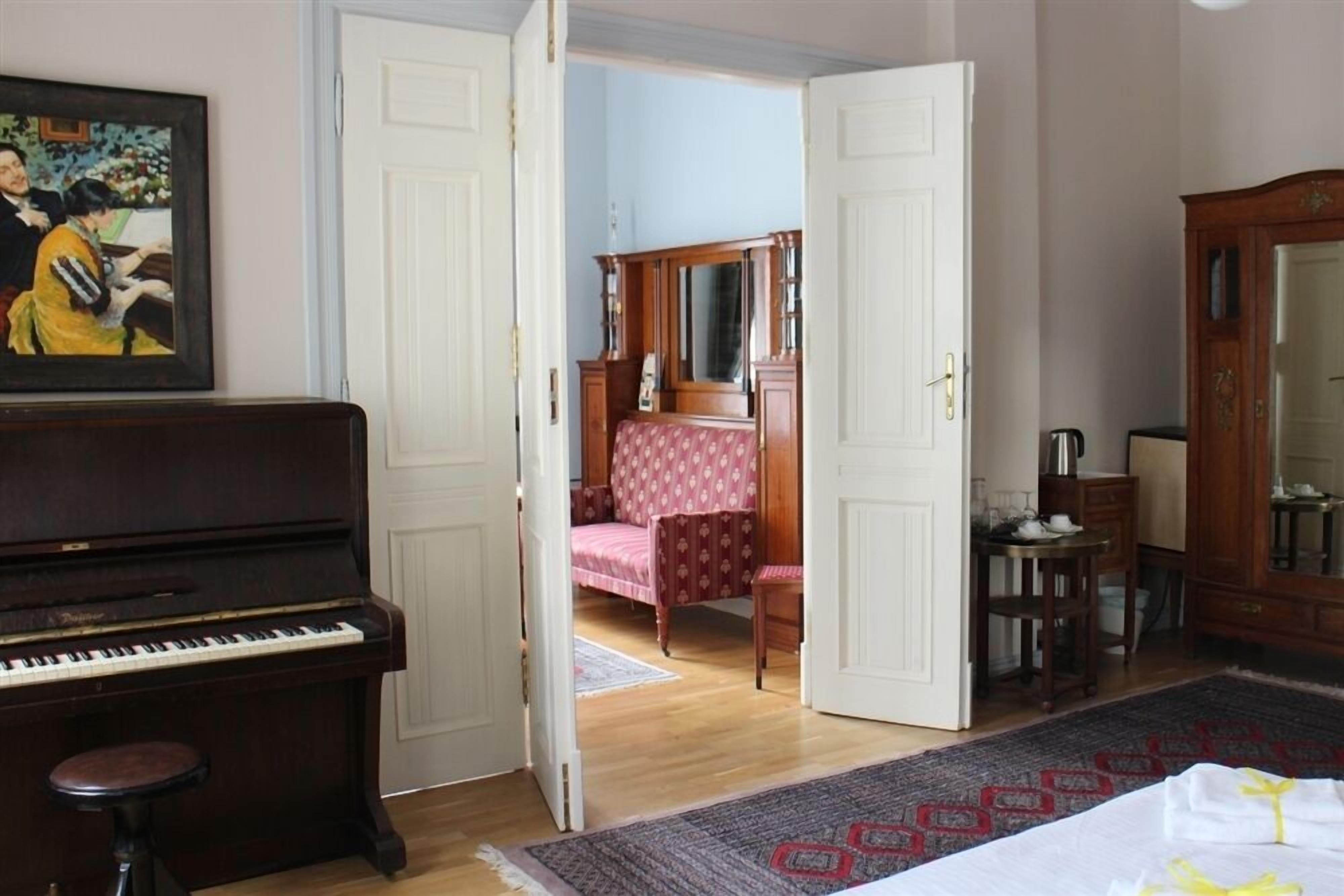 Une pièce avec un piano, un lit recouvert d’une couvre-lit à motifs, une chaise en bois et un meuble.