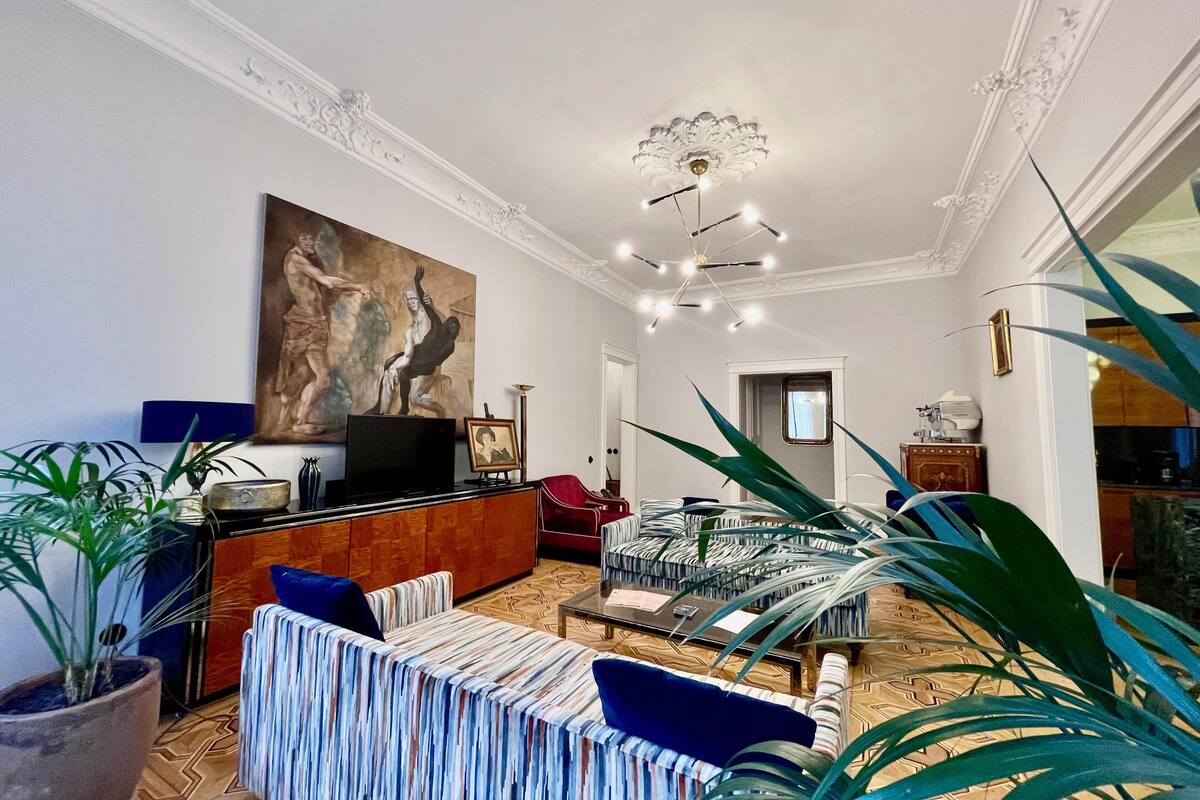 A spacious living room with a large painting, a television, and a dining area with a patterned rug.