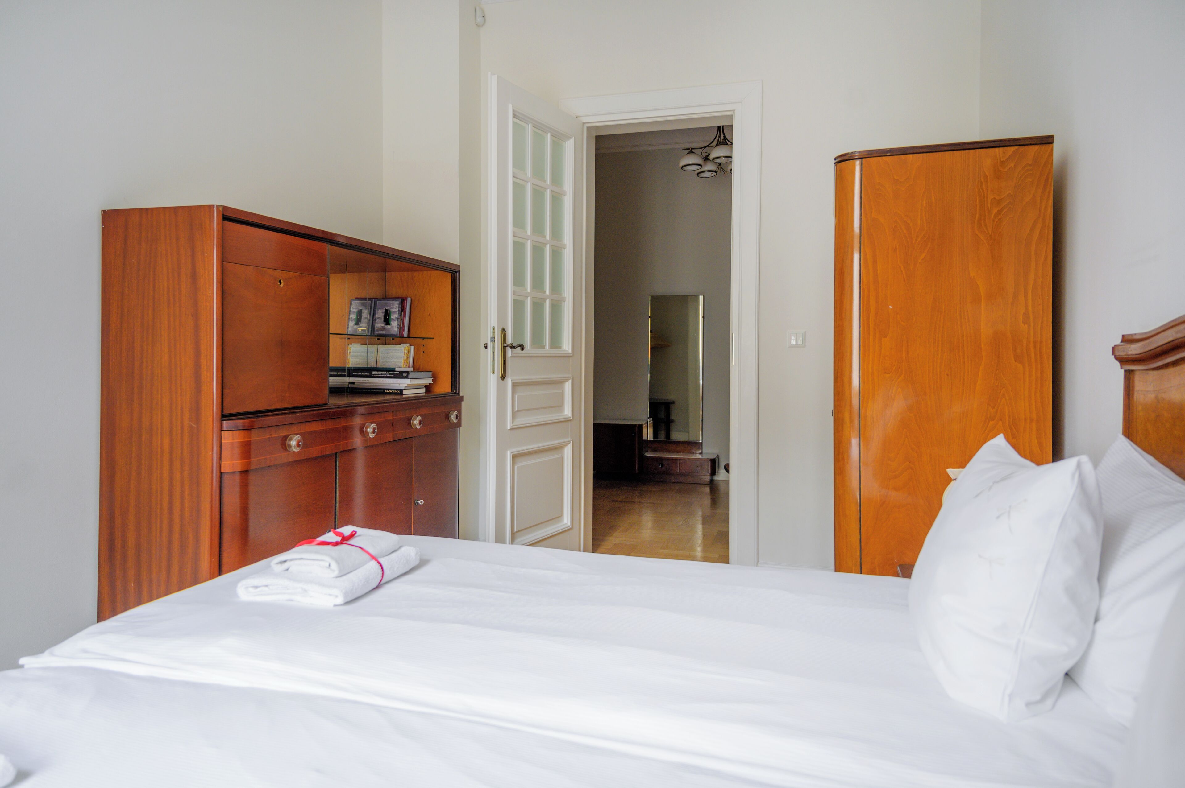 Habitación de hotel con una cama bien hecha, armario de madera y una puerta que da a un pasillo.