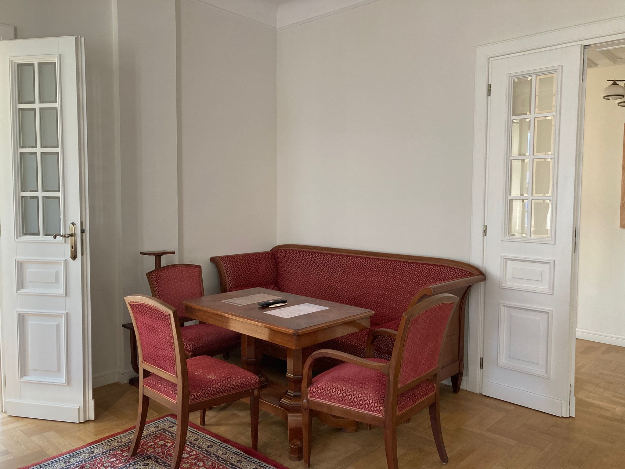 A corner dining area with a wooden table and four red upholstered chairs.