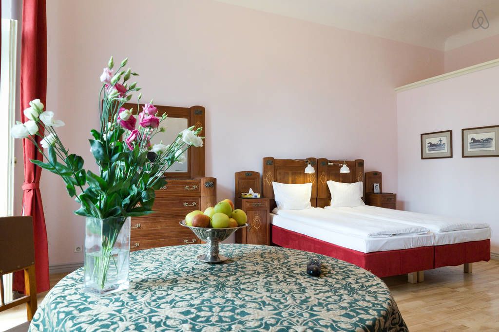 A bedroom with a bed, bedside table, and a vase with flowers and fruit.