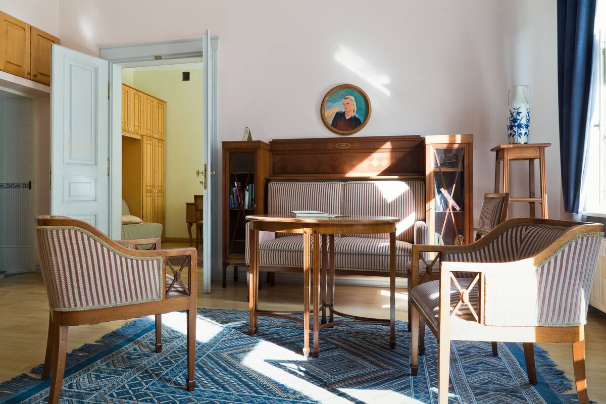 A room with a wooden chair, a table, a sofa, and a patterned rug.