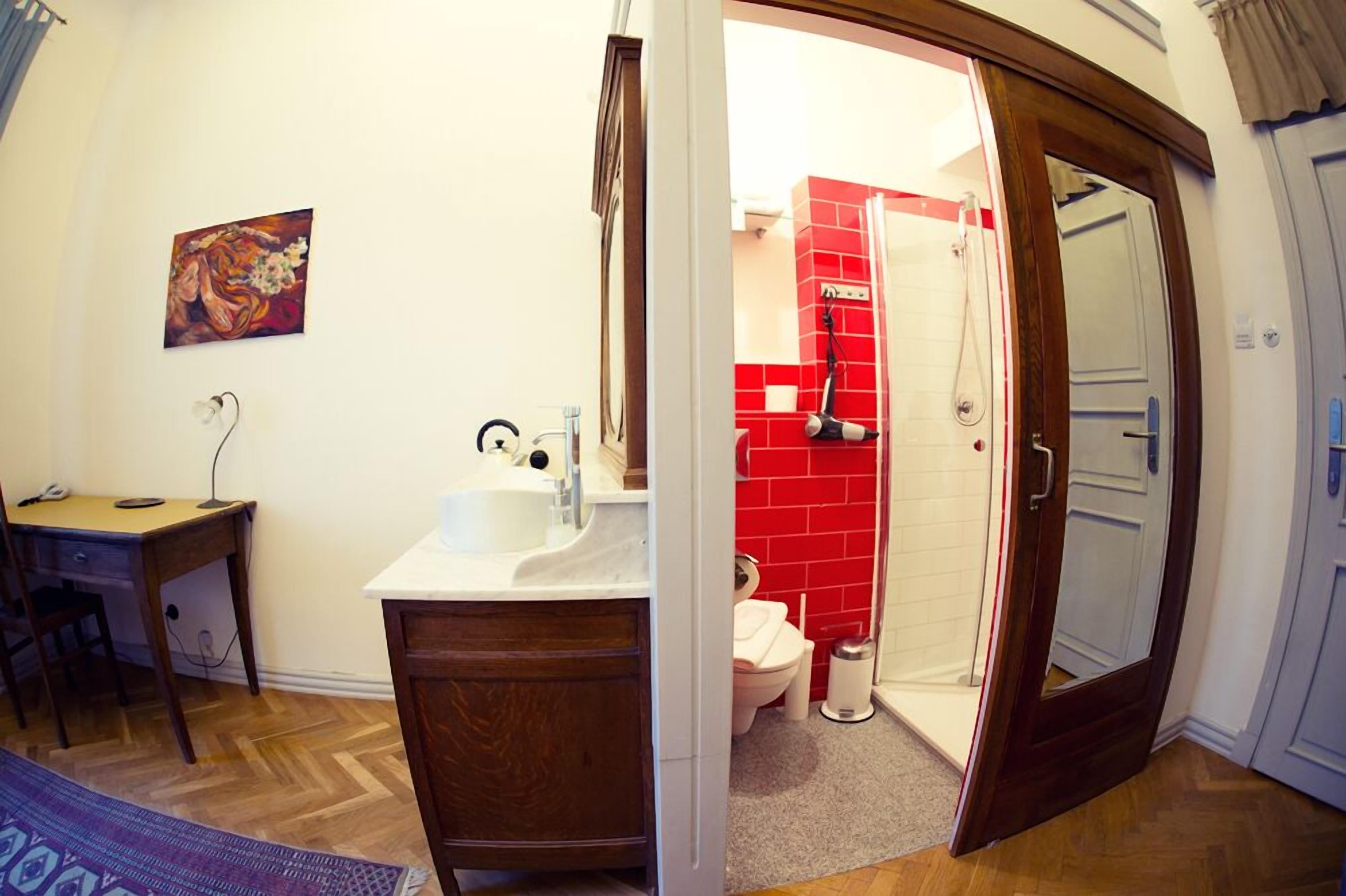 A bathroom with a white sink, a wooden desk, a painting on the wall, and a red-tiled shower area.