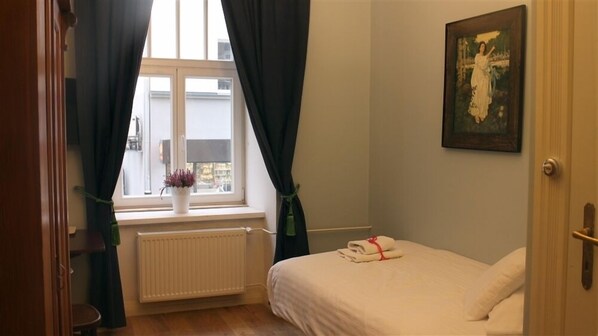 A bedroom with a bed, a radiator, a window with curtains, and a painting on the wall.