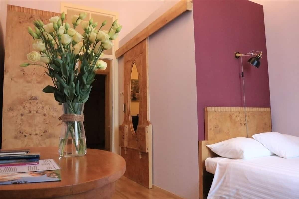 A hotel room with a wooden headboard, a bedside lamp, a bed with white linens, and a vase with flowers on a wooden table.